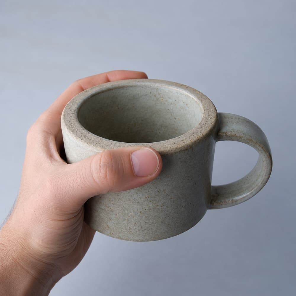 A hand holding the Thick-Wall Mug 320 ml, showing the scale of the cup against a hand
