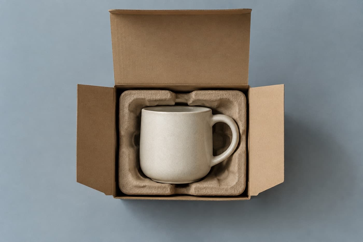 A stoneware mug inside an open kraft cardboard box packed with moulded pulp cushioning