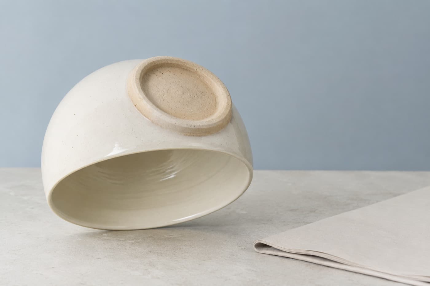 A stoneware cup turned upside down showing its unglazed foot ring, beside a folded paper document